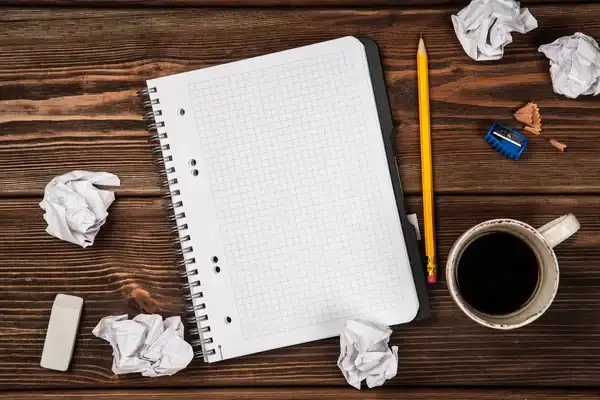 cuaderno en blanco con hojas arrugadas a su costado hechas en un bloqueo creativo