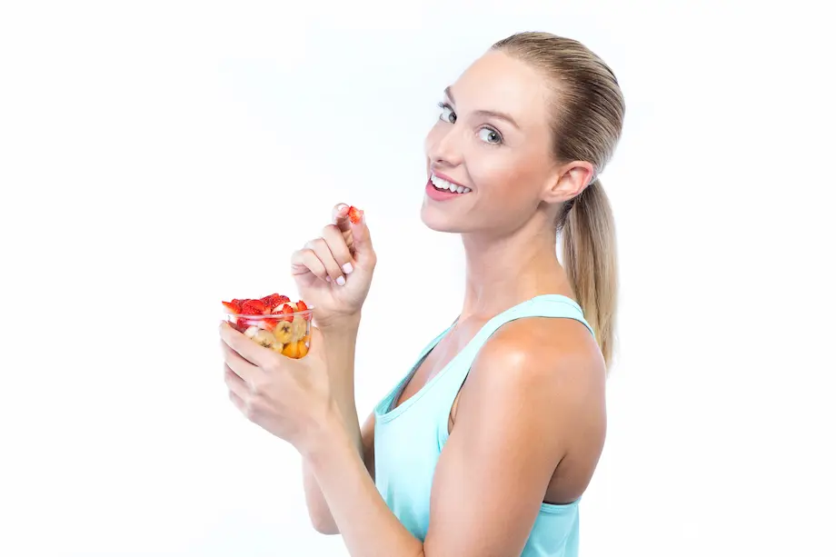 Joven y bella mujer comiendo cereales y frutas sobre fondo blanco.
