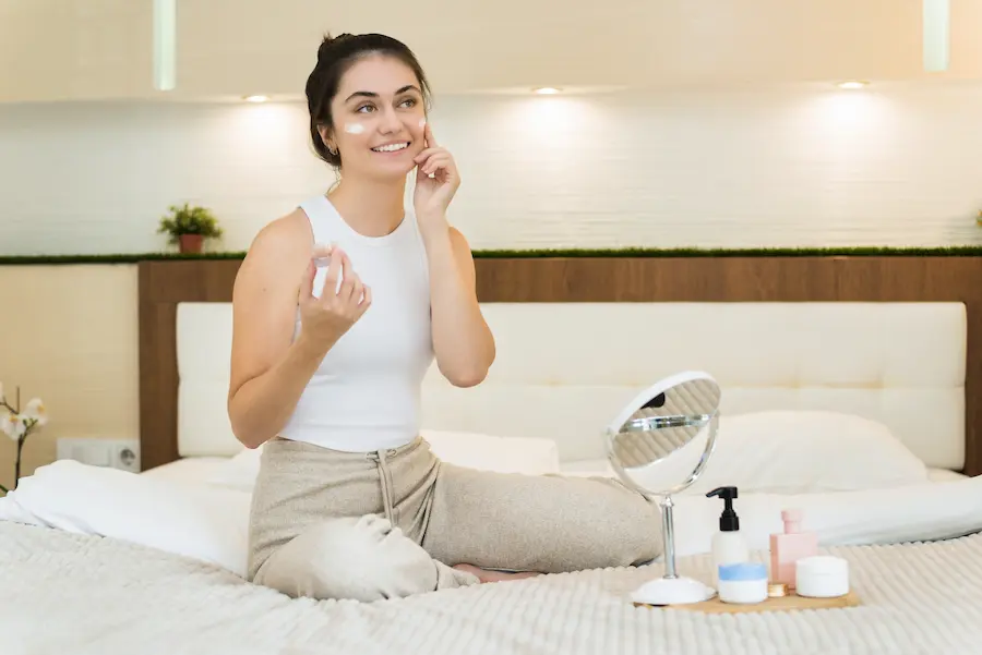 mujer sentada en la cama realizandose una limpieza en la cara