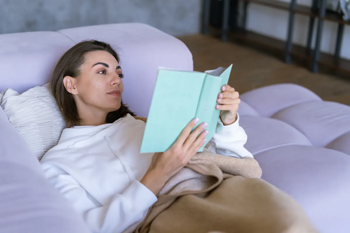 chica recostada en el sofa con un libro en la mano