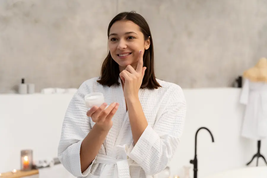 mujer-joven-aplicar-crema-hidratante-en-el-rostro-antes-de-tomar-un-bano