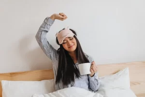 Mujer de pelo largo en pijama azul se estira dulcemente después de dormir
