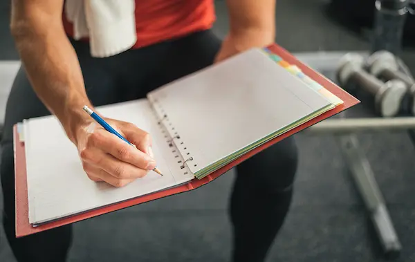 Hombre anotando su progreso en una libreta, consejos para mantener la motivación en ejercicios para hombres
